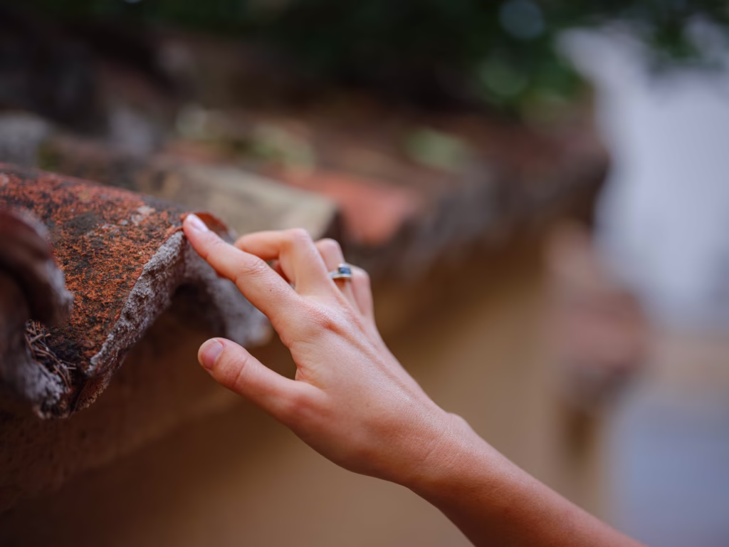 A close-up view of a woman's hand touching a weathered terracotta roof tile, showcasing potential wear areas needing tile roof maintenance and repair chimney leak in your Ocala Home.